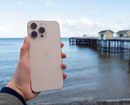 A hand holding an iPhone 16 Pro Max in front of a coastal landscape
