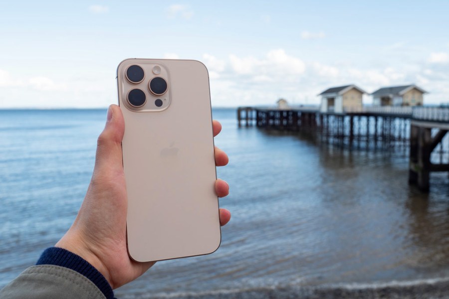 A hand holding an iPhone 16 Pro Max in front of a coastal landscape