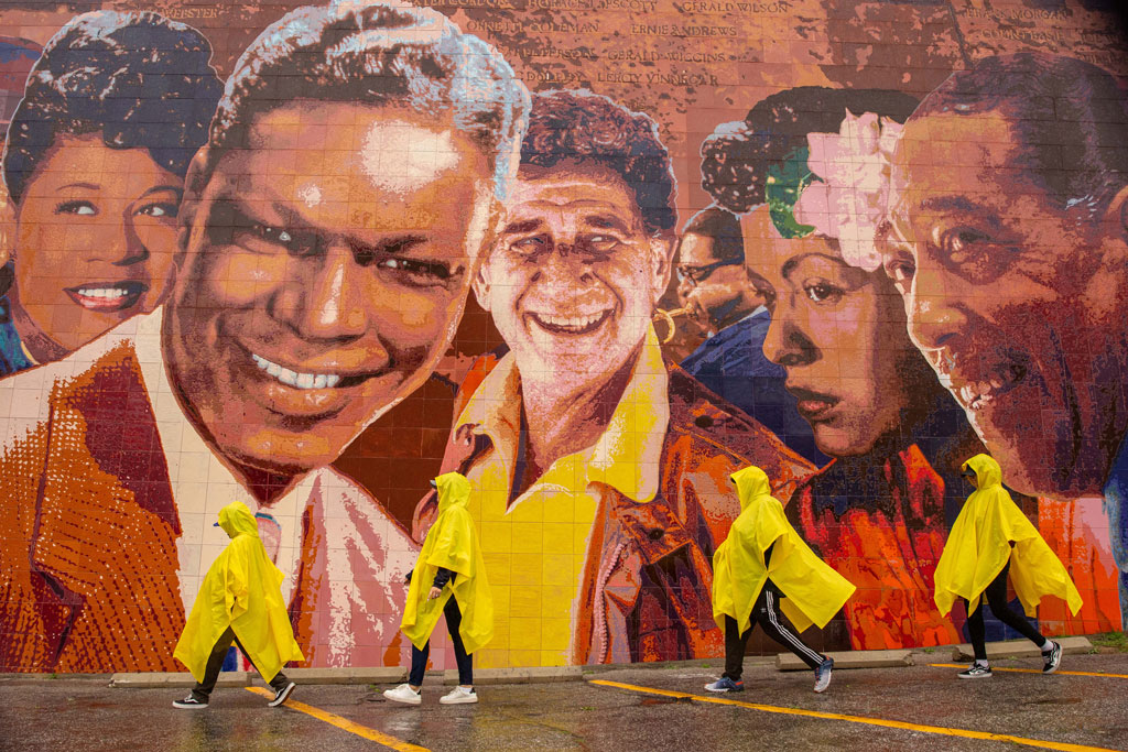 Los Angeles, four people dressed in yellow raincoats walk past a mural of jazz singers