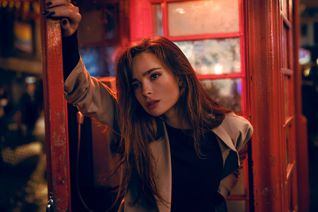 low light portrait of a woman in a red telephone box