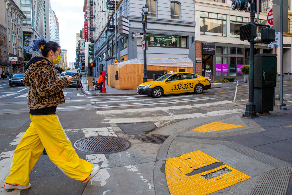 San francisco busy street with a woman crossing in yellow pants, and a yellow cab passing by, street photography America