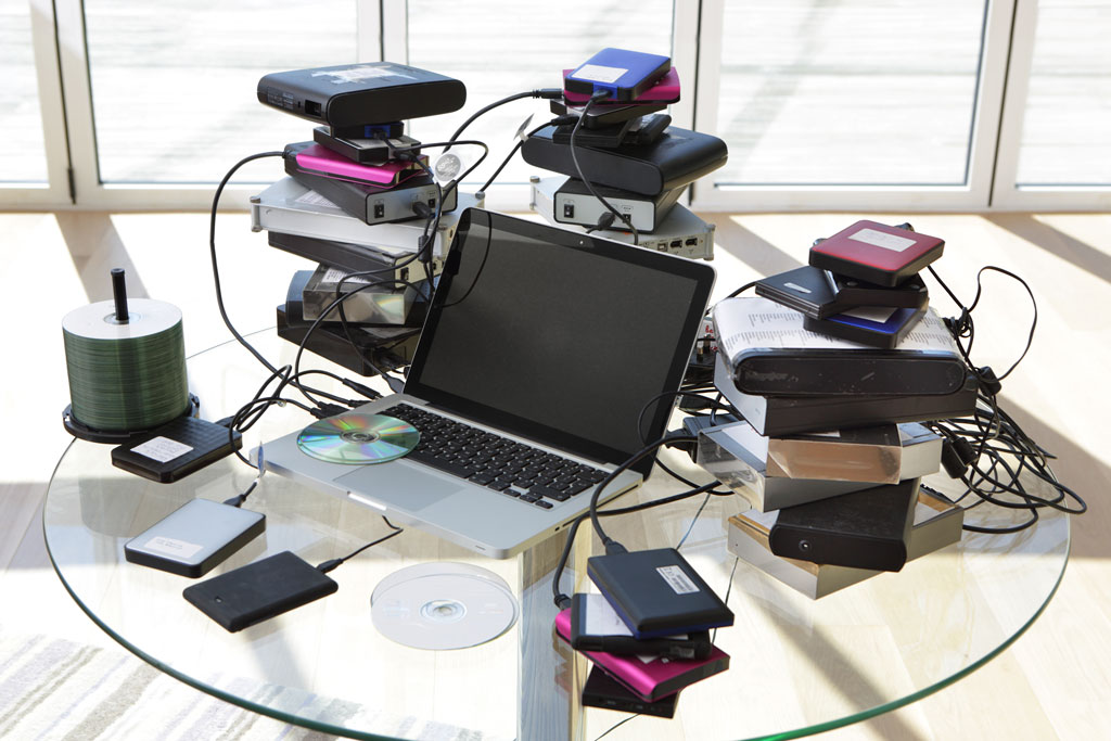 A laptop on a table surrounded by piles of external harddrives