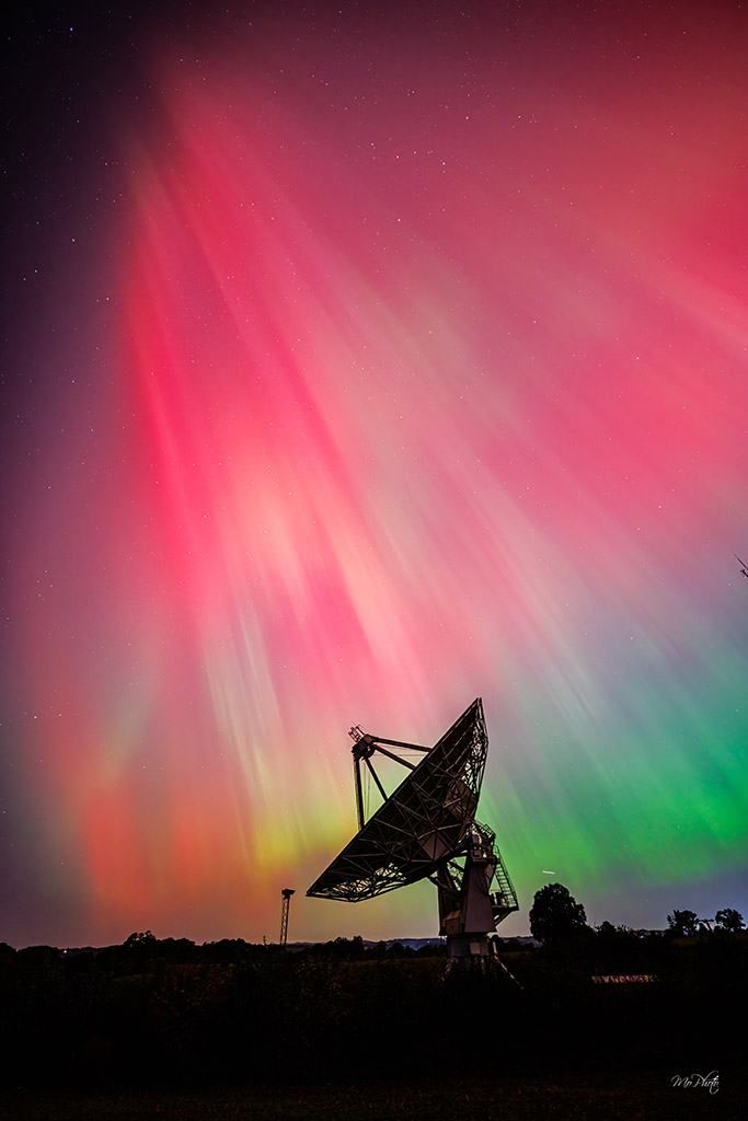 aurora borealis over silhouette of radio telescope