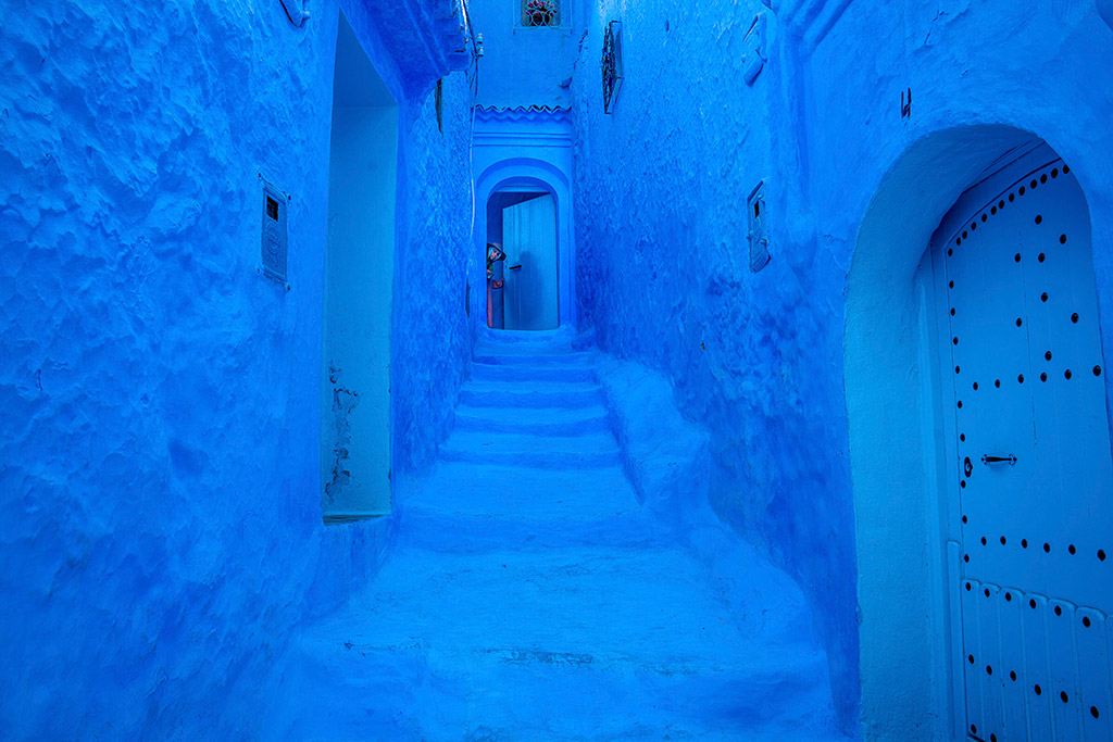 blue buildings and steps leading to a doorway with person peering through