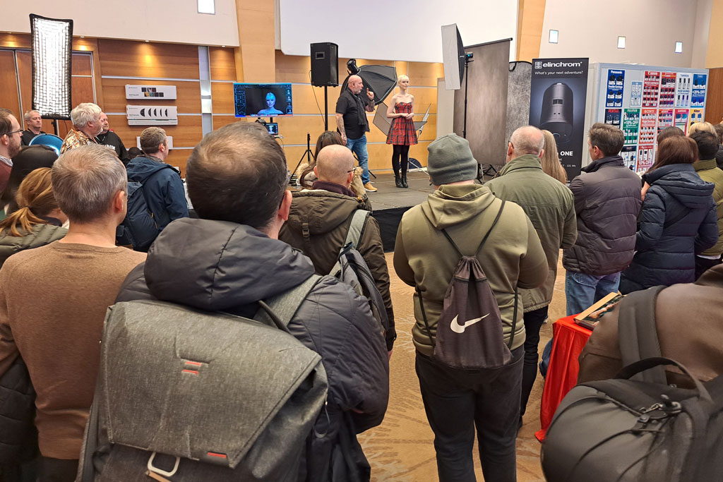 People standing watching a photography technique demonstration at a photgraphy show