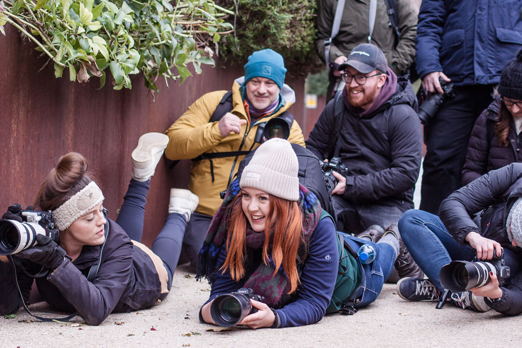 A group of people with cameras in hand, some laying on the floor, some crouching or standing