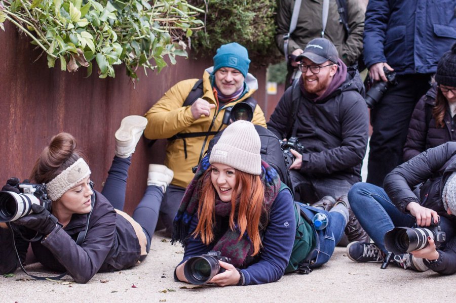 A group of people with cameras in hand, some laying on the floor, some crouching or standing