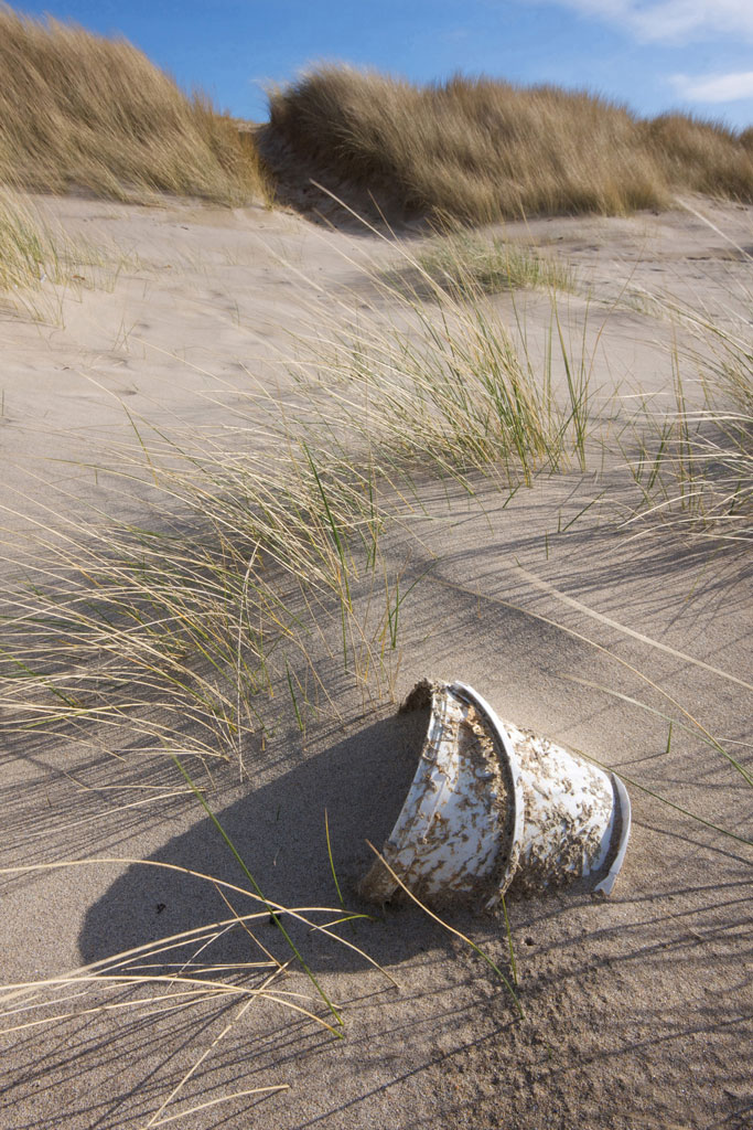 a plastic bucket half buried on the beach