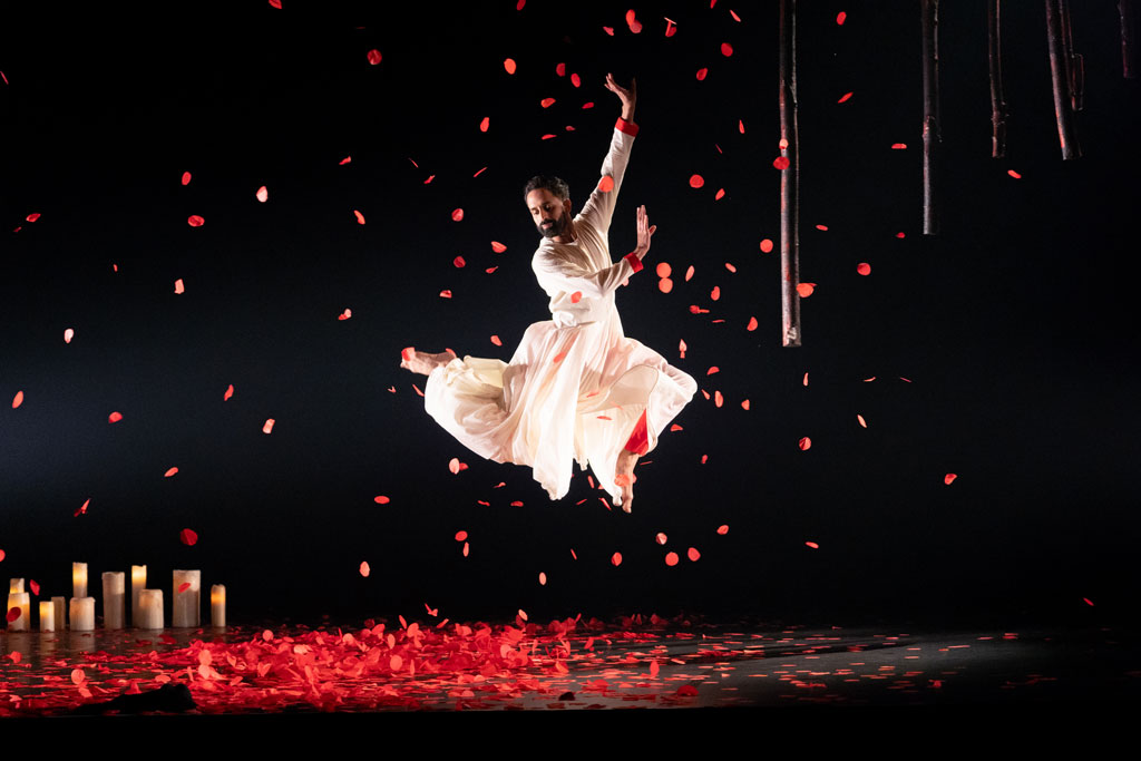 a man in a white attire leaps to the air, red flower petals flew in the air