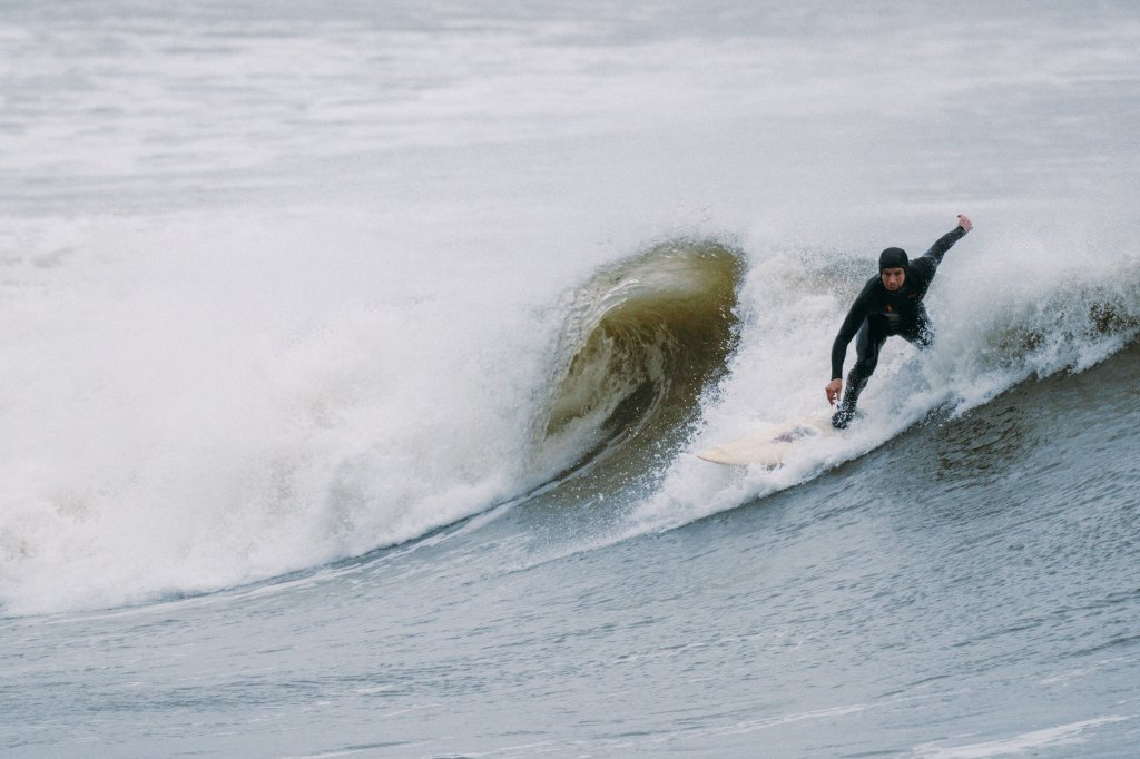 A surfer in a wetsuit rides a wave