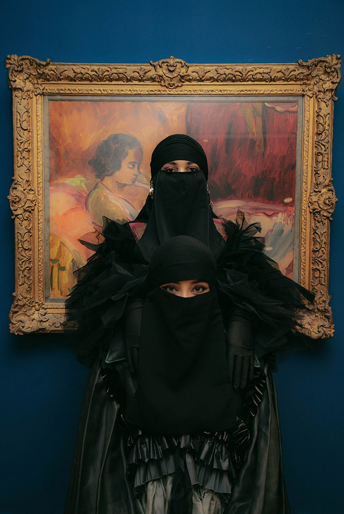 portrait shows two women wearing a Burqa and Niqab in front of a gilt frame artwork