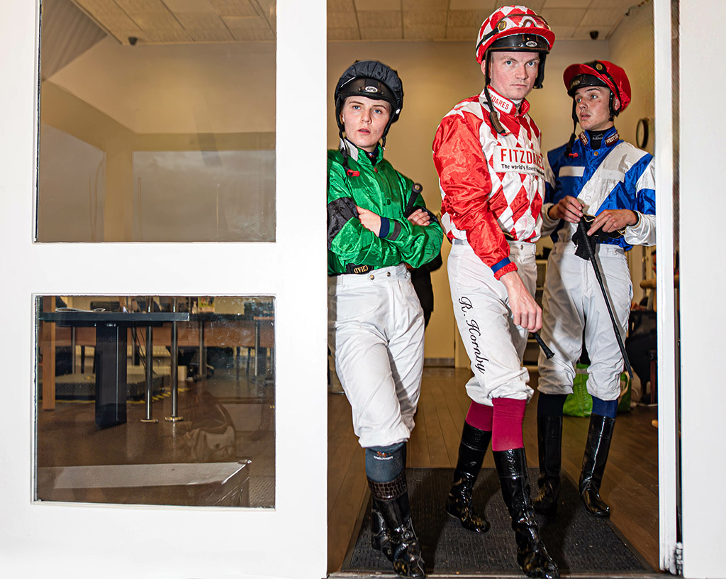 portrait of three jockeys in bright colours stood in a doorway