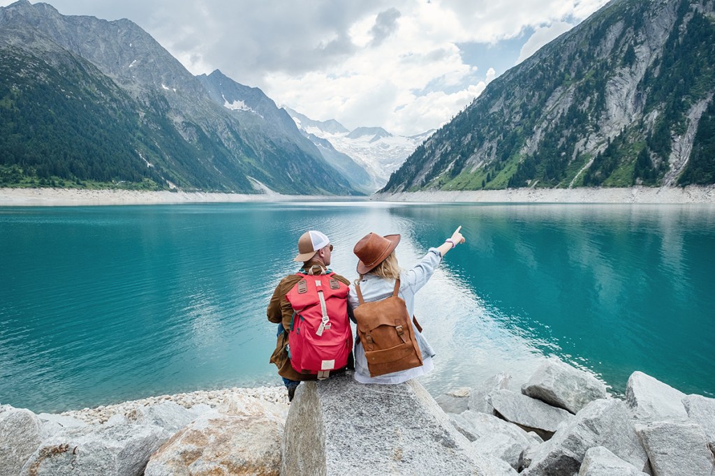 a couple sat on a rock looking at a lake and mountains