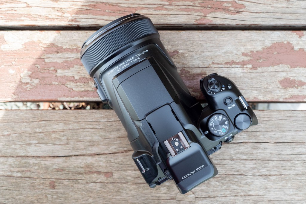 The Nikon Coolpix P1100 on a wooden surface, shot from above