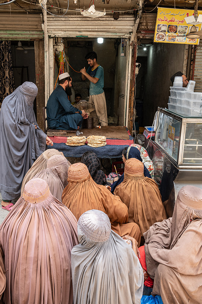 Afghan women sit and wait for free bread handouts at the market