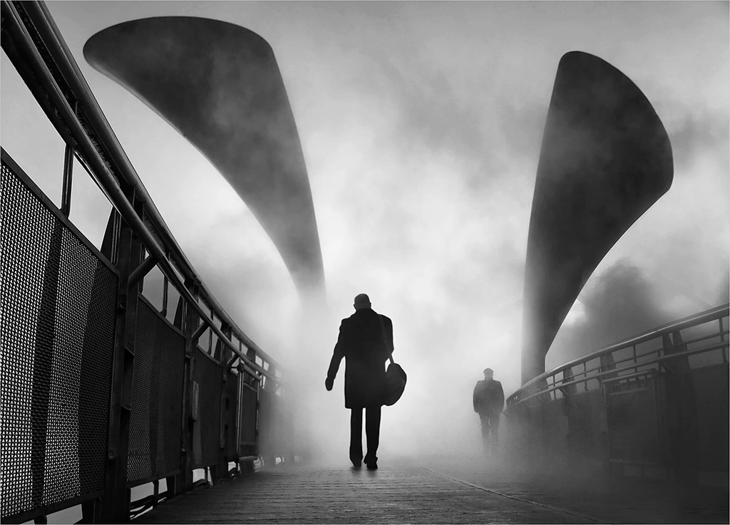 Silhouette of a person walking along a bridge surrounded by mist