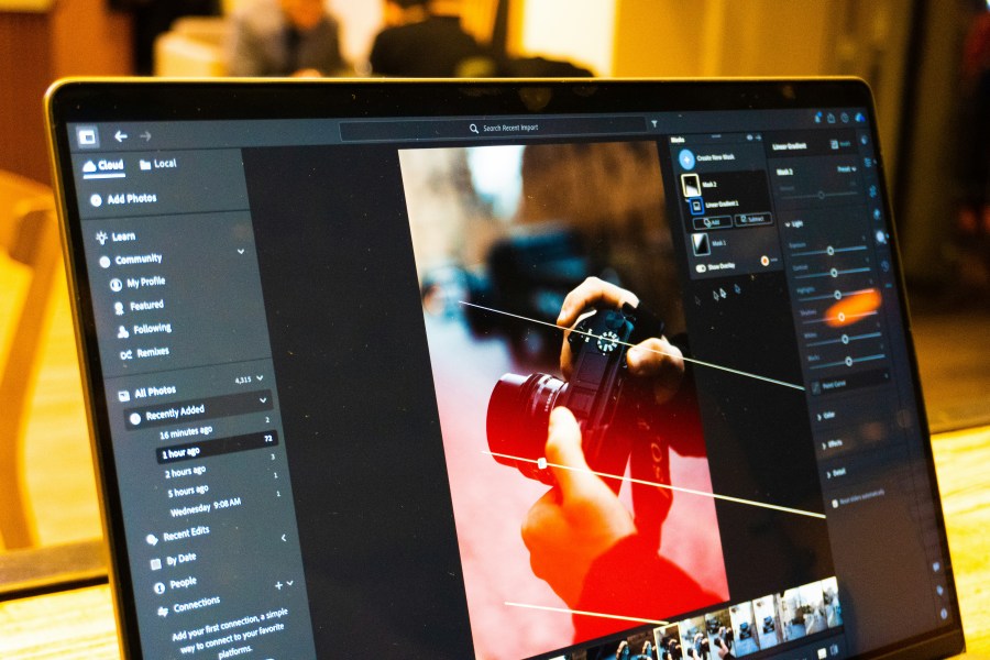 Photograph of laptop with photo editing software open being used to edit a photograph of hands holding a camera.