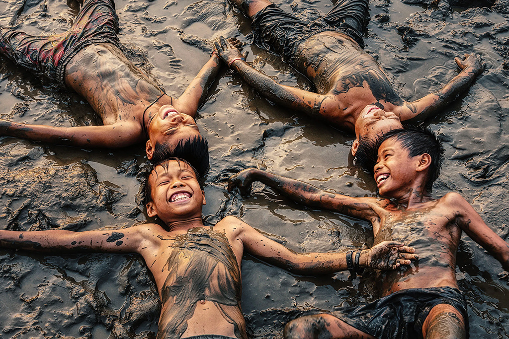 four young boys lying in mud