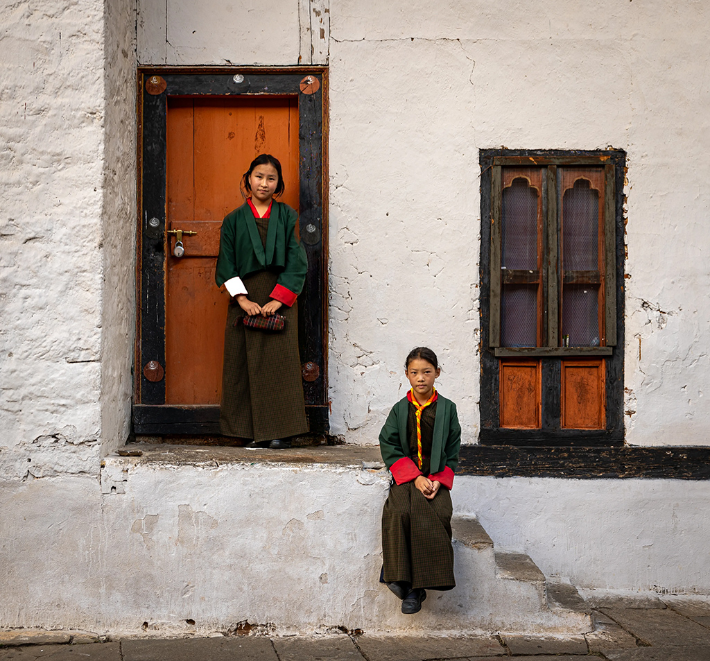 Bhutanese schoolgirls stood infront of white building with orange doors