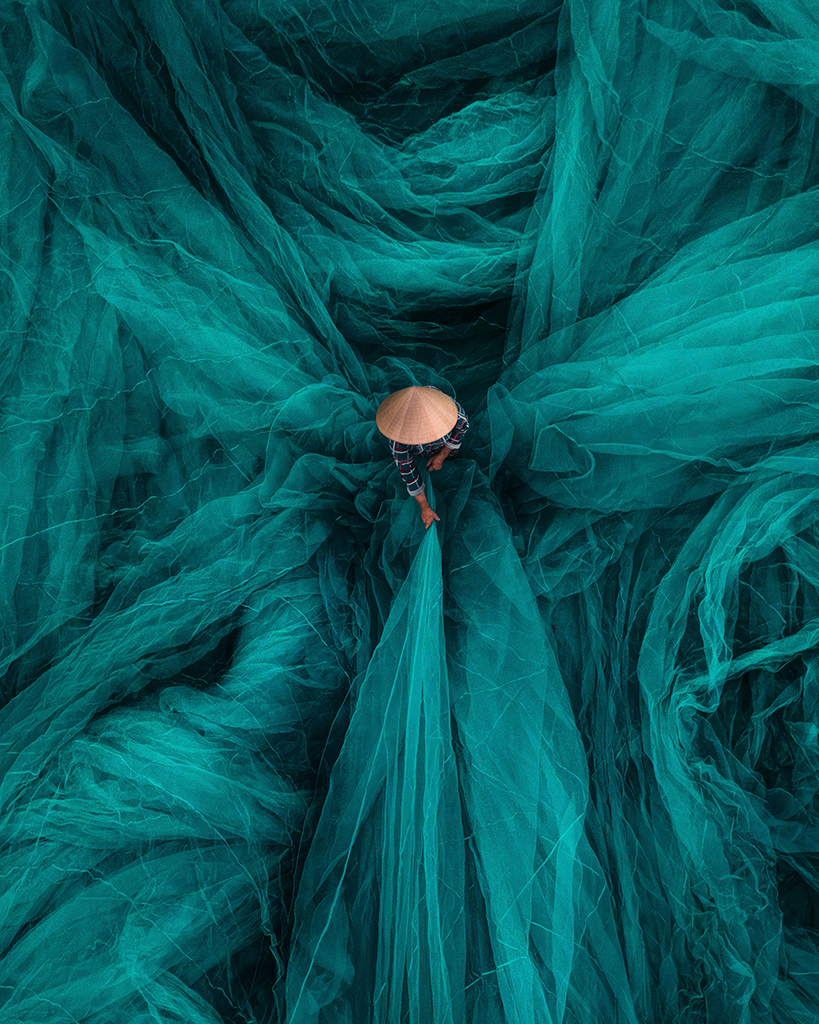 Chris Ha, United States, Threads of Tradition, A Vietnamese artisan weaves a fishing net by hand, surrounded by flowing green threads, a tradition passed down through generations. 2025 International Aerial Photographer of the Year Award – Top 101 Photographs

