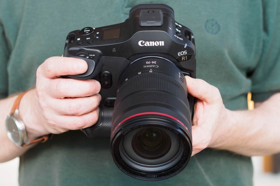 Canon EOS R1 full-frame mirrorless camera held in hand, with 24-70mm lens attached.