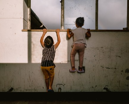 Children peer out of a broken window overlooking the courtyard at Cissie Gool House