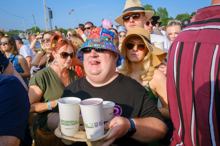 man at a festival wearing a bucket hat carrying container of paper cups