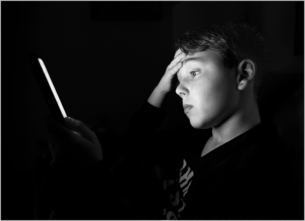 Young boy with hand on his forehead looking at a screen