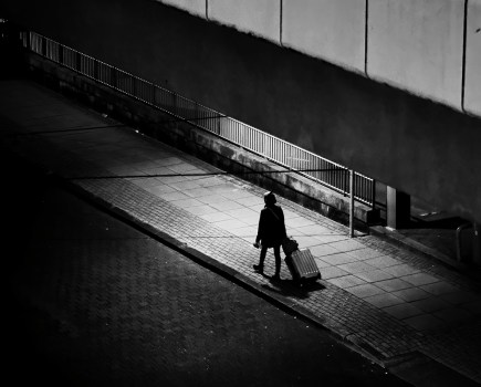 single person in patch of light in the middle of shadows on the street