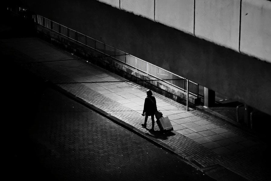single person in patch of light in the middle of shadows on the street