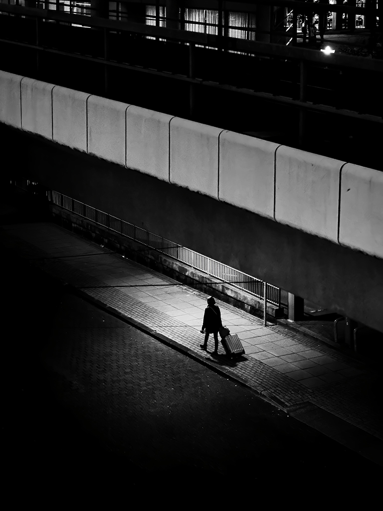 single person in patch of light in the middle of shadows on the street