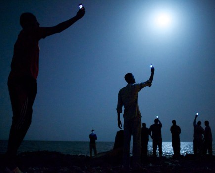 African migrants on the shore of Djibouti City raise phones in an attempt to catch an inexpensive signal from neighboring Somalia. Image Credit: John Stanmeyer, USA, VII SINGLE USE ONLY