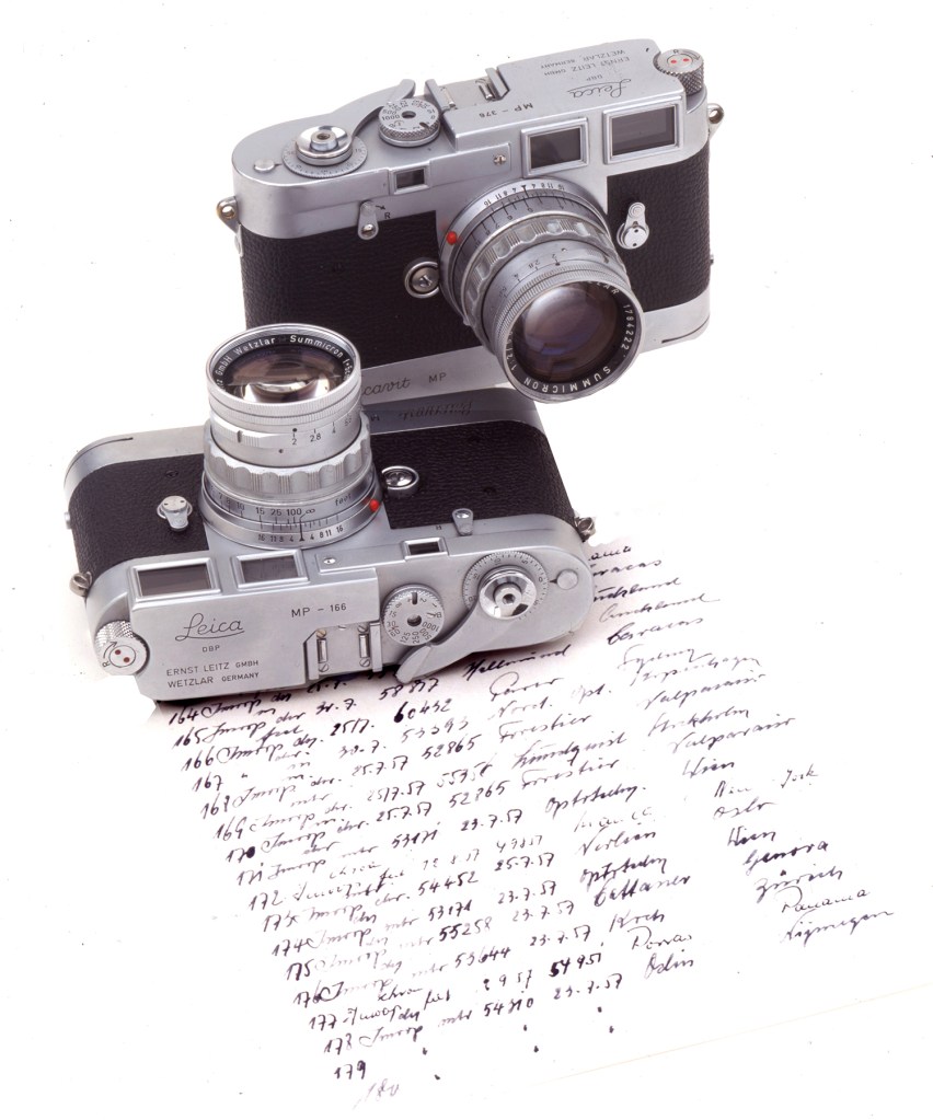 Leica MP cameras stand on a page from Leitz sales ledgers in which hand-written details of every camera and its destination were listed