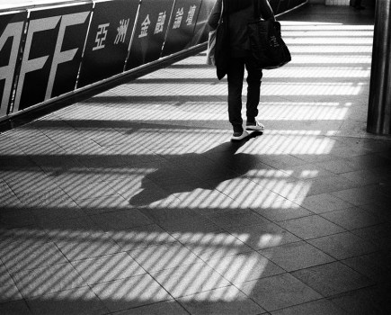 street photo of someone walking along a bridge in between shadows