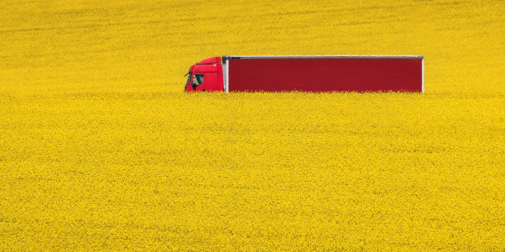 red lorry against yellow rapeseed plant field