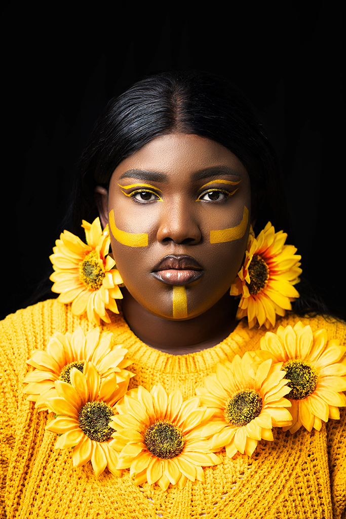 woman in yellow with yellow face markings wearing sunflower earrings and necklace
