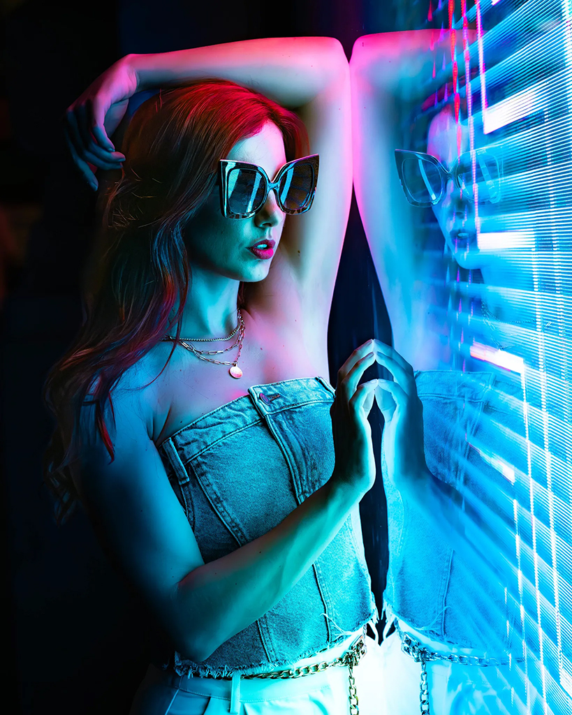 portrait of a woman in glasses leaning against neon colour lights