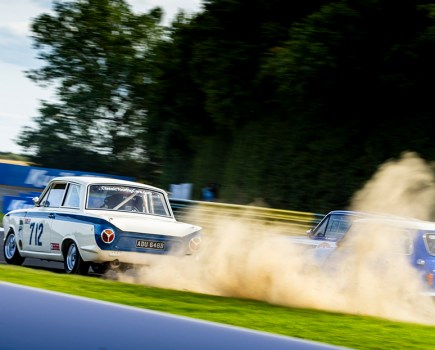 photo of two blue and white cars racing on a track with smoke coming out the back