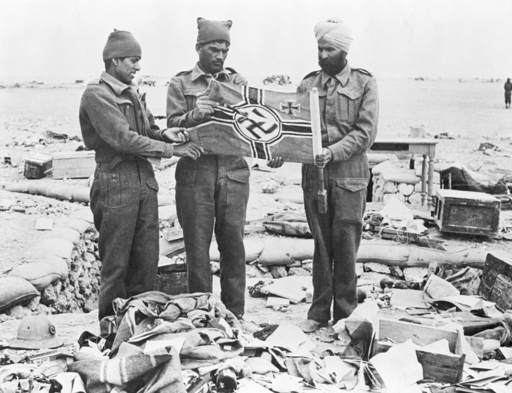 (Original Caption) 1/5/42-Libya: British Indian troops examine a Nazi flag found among the rubble in the shallow axis trenches on the Western Desert. This picture was made after the capture of Libyan Omar.