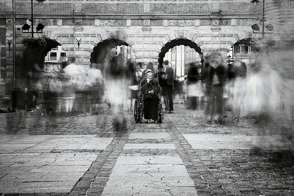 woman in wheel chair surrounded by people walking past long exposure