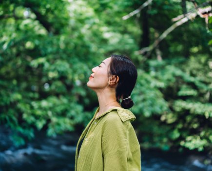 Woman meditating in nature with her eyes closed, setting herself free and feeling relieved. Enjoying fresh air and breathing in the calmness with head up. Freedom in nature. Connecting with nature. Health and wellness concept