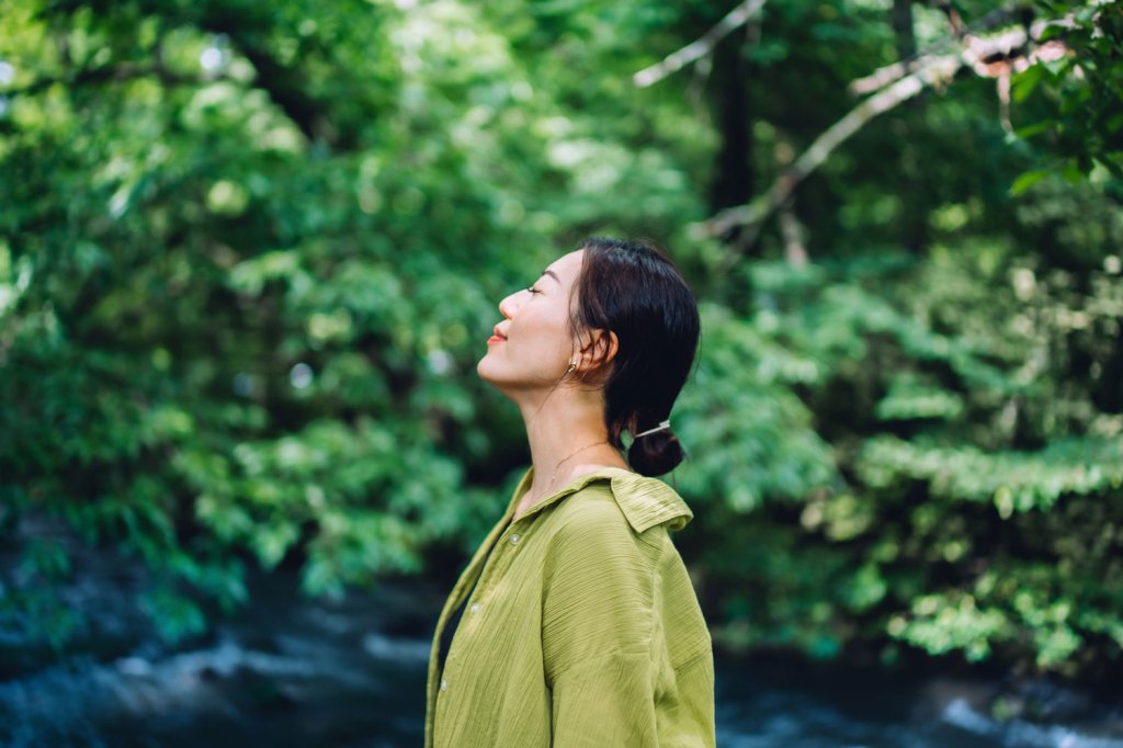 Woman meditating in nature with her eyes closed, setting herself free and feeling relieved. Enjoying fresh air and breathing in the calmness with head up. Freedom in nature. Connecting with nature. Health and wellness concept