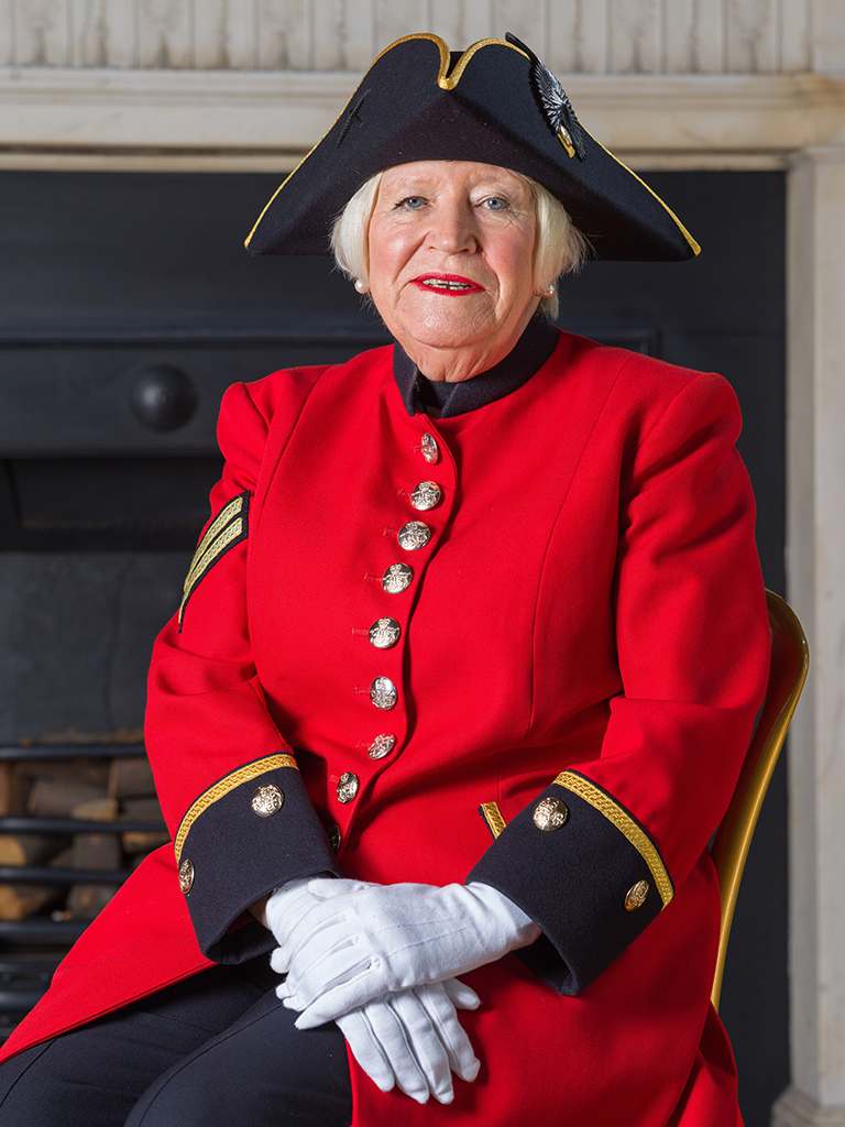 close up portrait of an older woman in red coat uniform and black hat