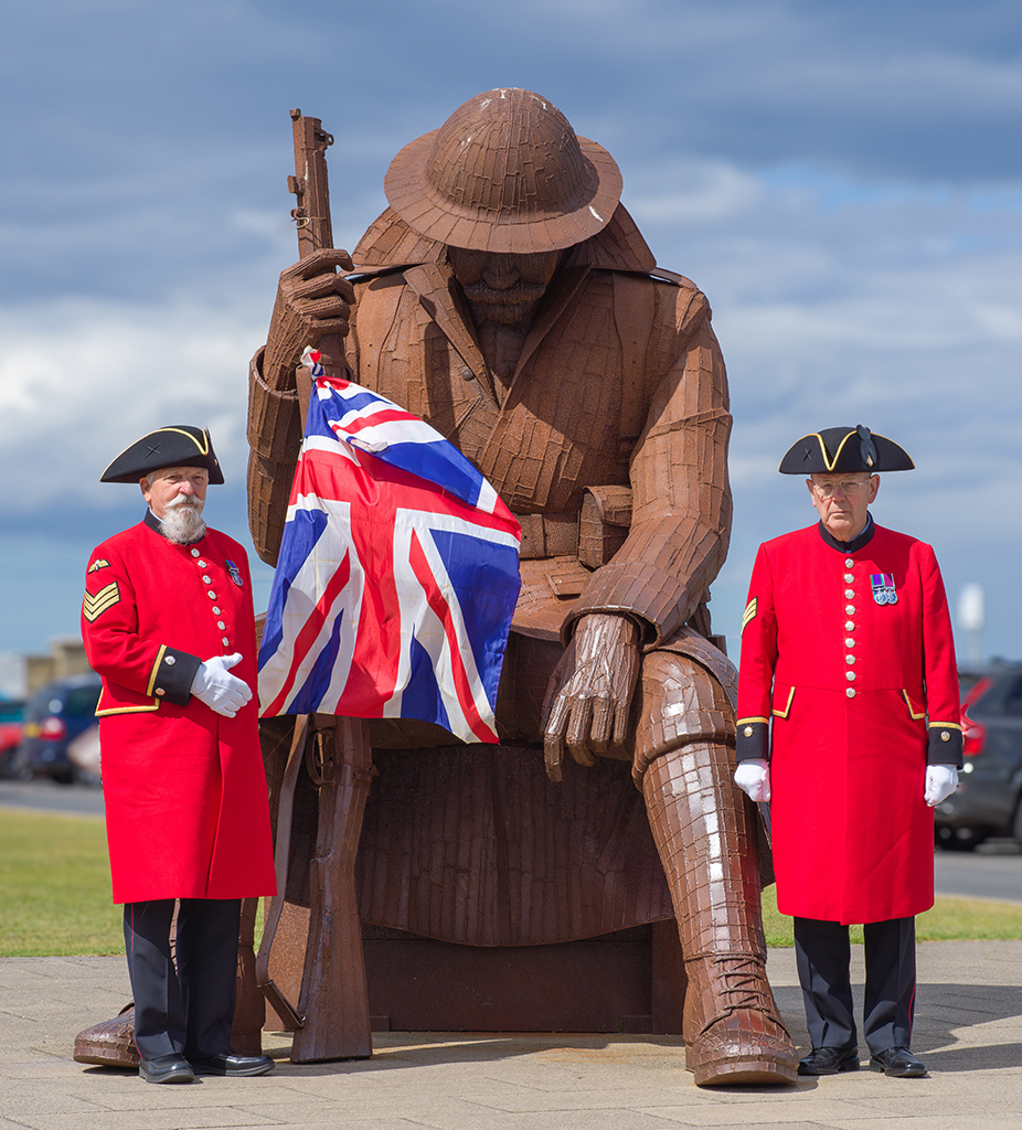 two older men in red coat uniform stood with army statue