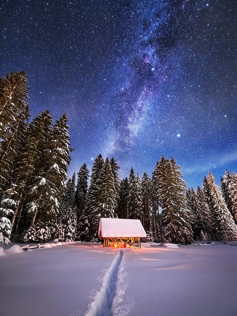 low light snow scene with a hut and milky way sky in the background
