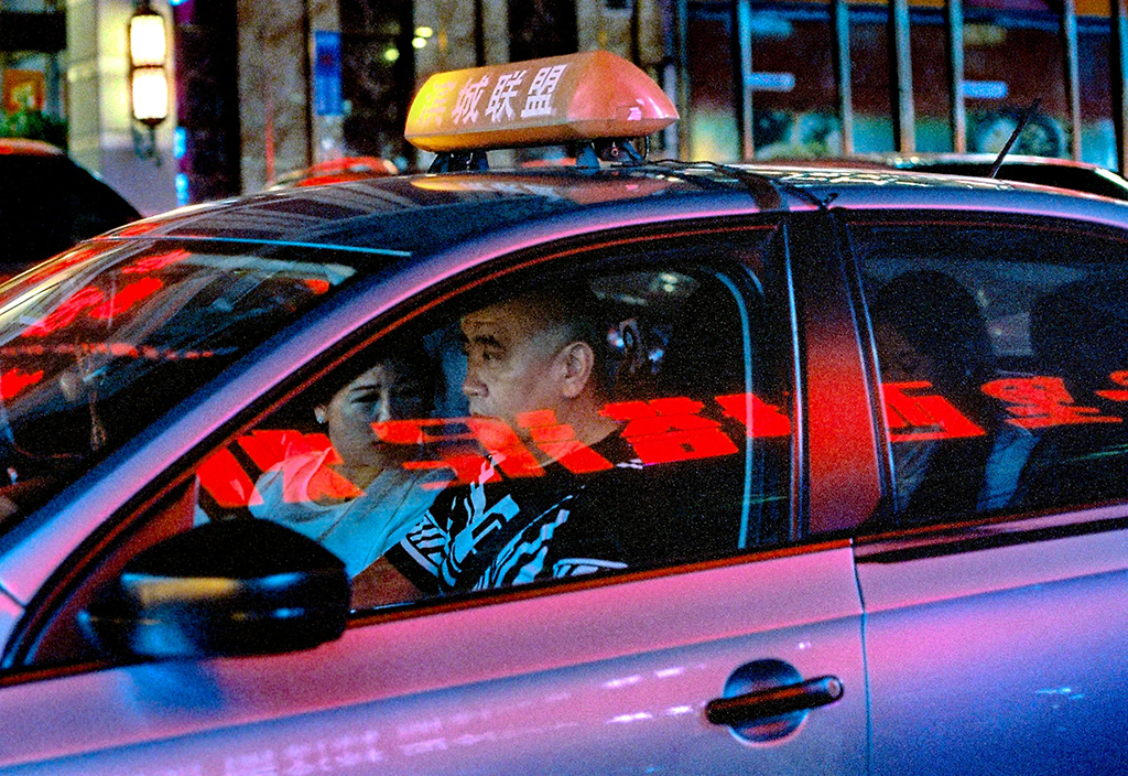 film photograph of a night time close up of a taxi with neon lights reflecting