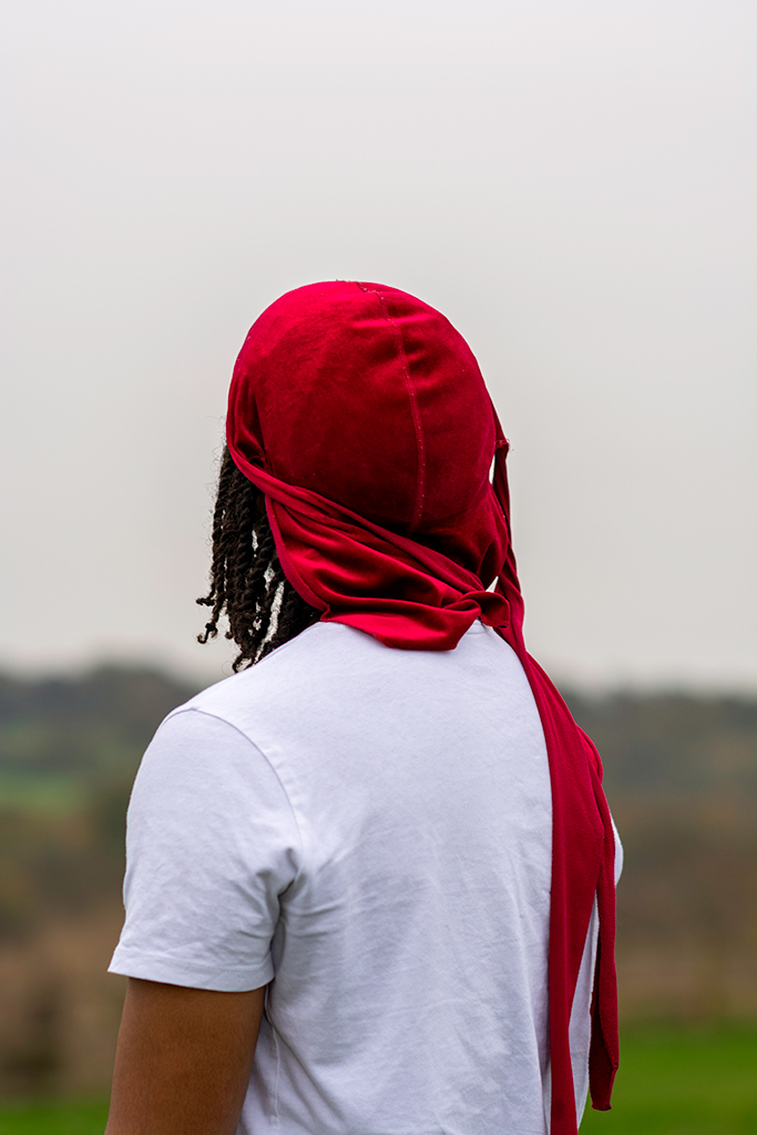 portrait of a person facing a white wall with a red scarf on their head