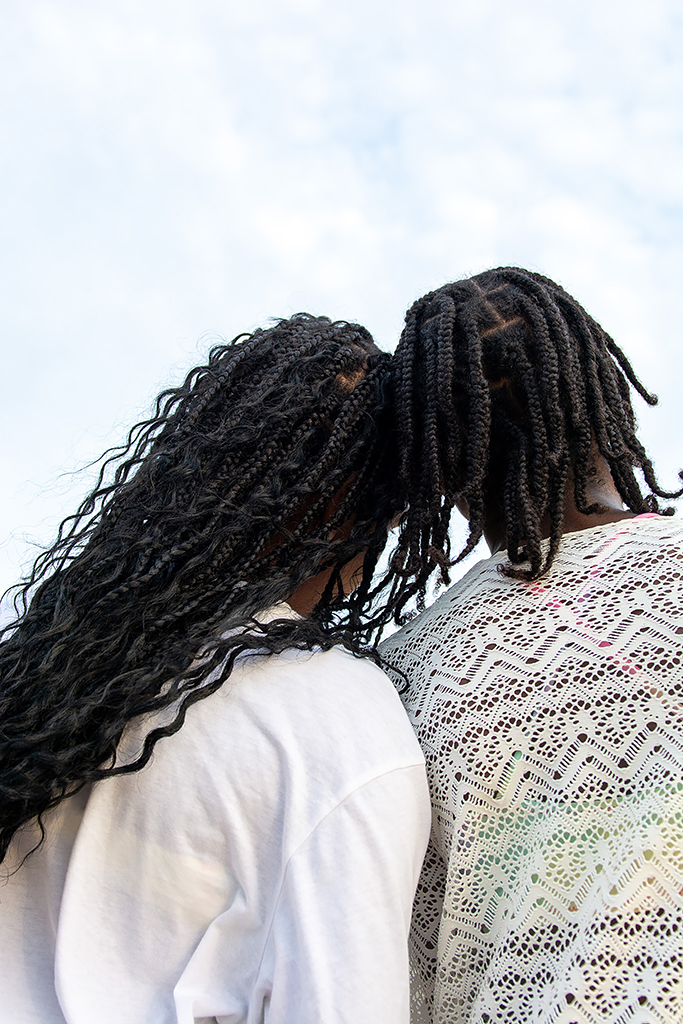 portrait of two people facing away from the camera leaning their heads against eachother