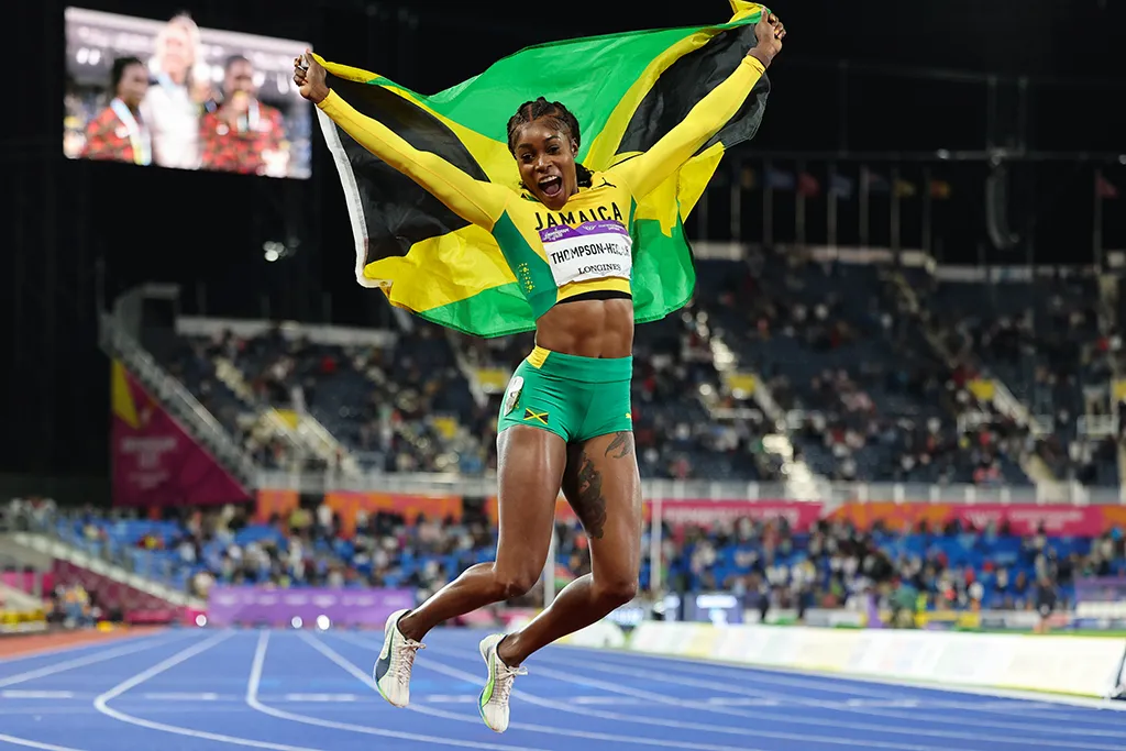 photo of a jamaican athlete jumping mid-air on a track with flag