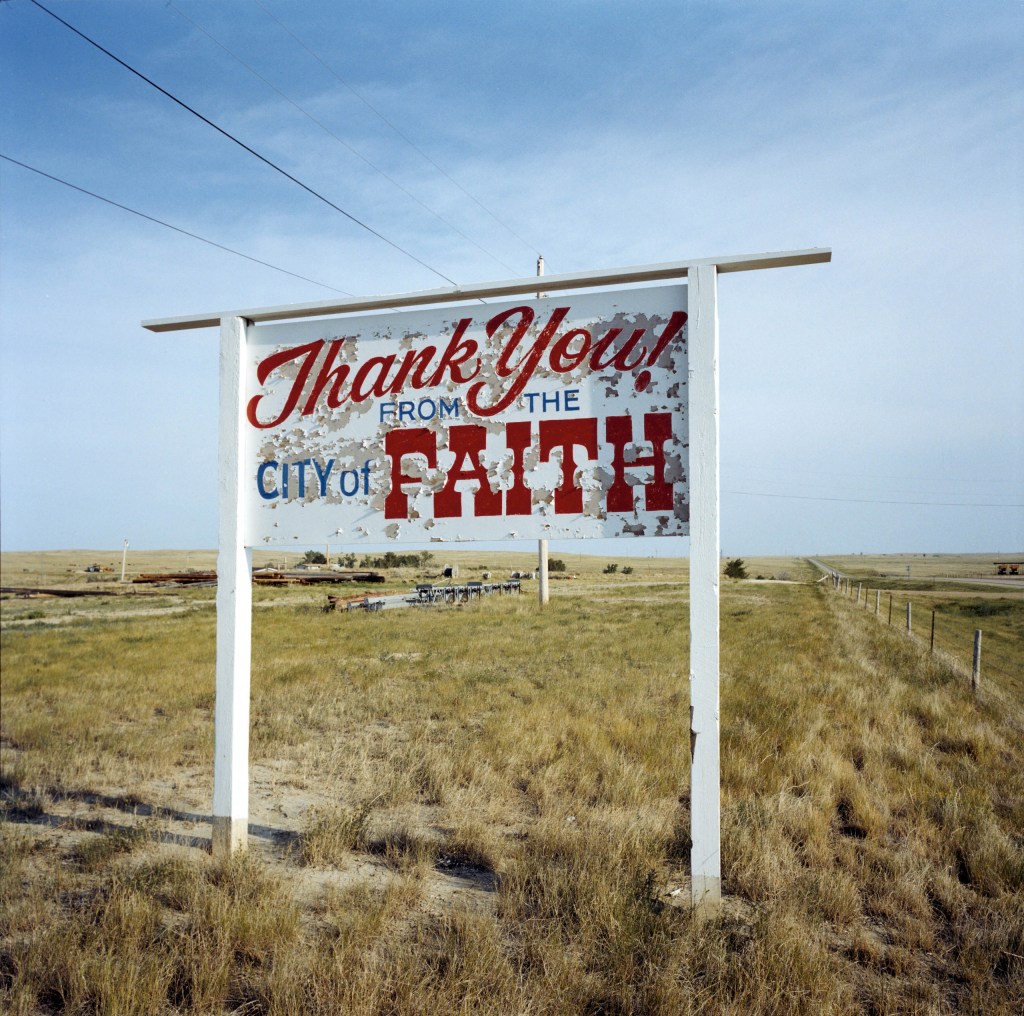 A sign for those leaving Faith behind, South Dakota, USA, 2002. Image Credit: Peter Dench